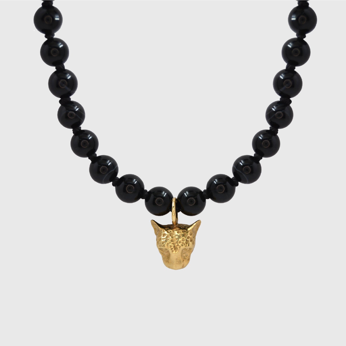 Black beaded necklace with a gold pendant on a light gray background
