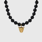 Black beaded necklace with a gold pendant on a light gray background