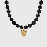 Black beaded necklace with a gold pendant on a light gray background