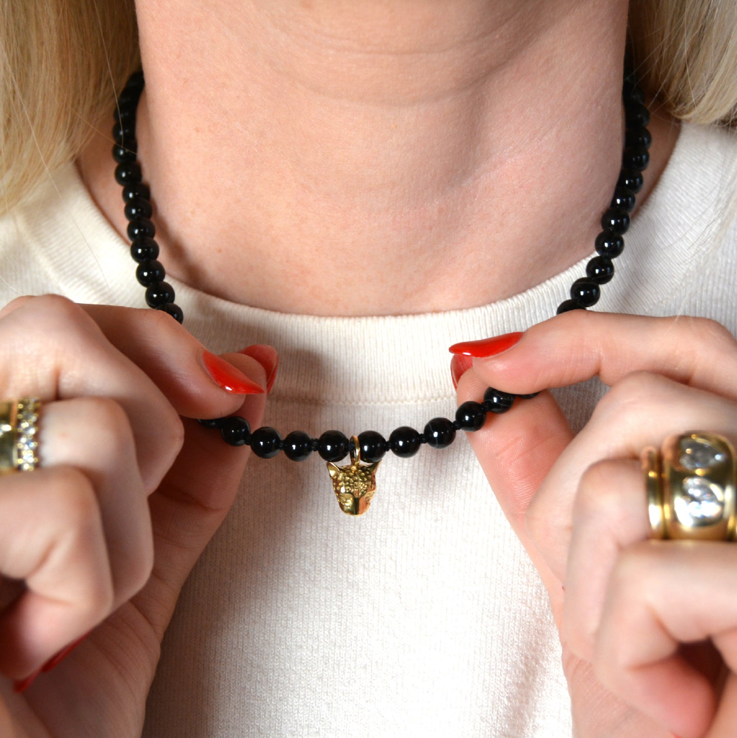 Person holding a black beaded necklace with a gold pendant