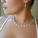 Close-up of a person wearing a silver chain necklace and hoop earring.