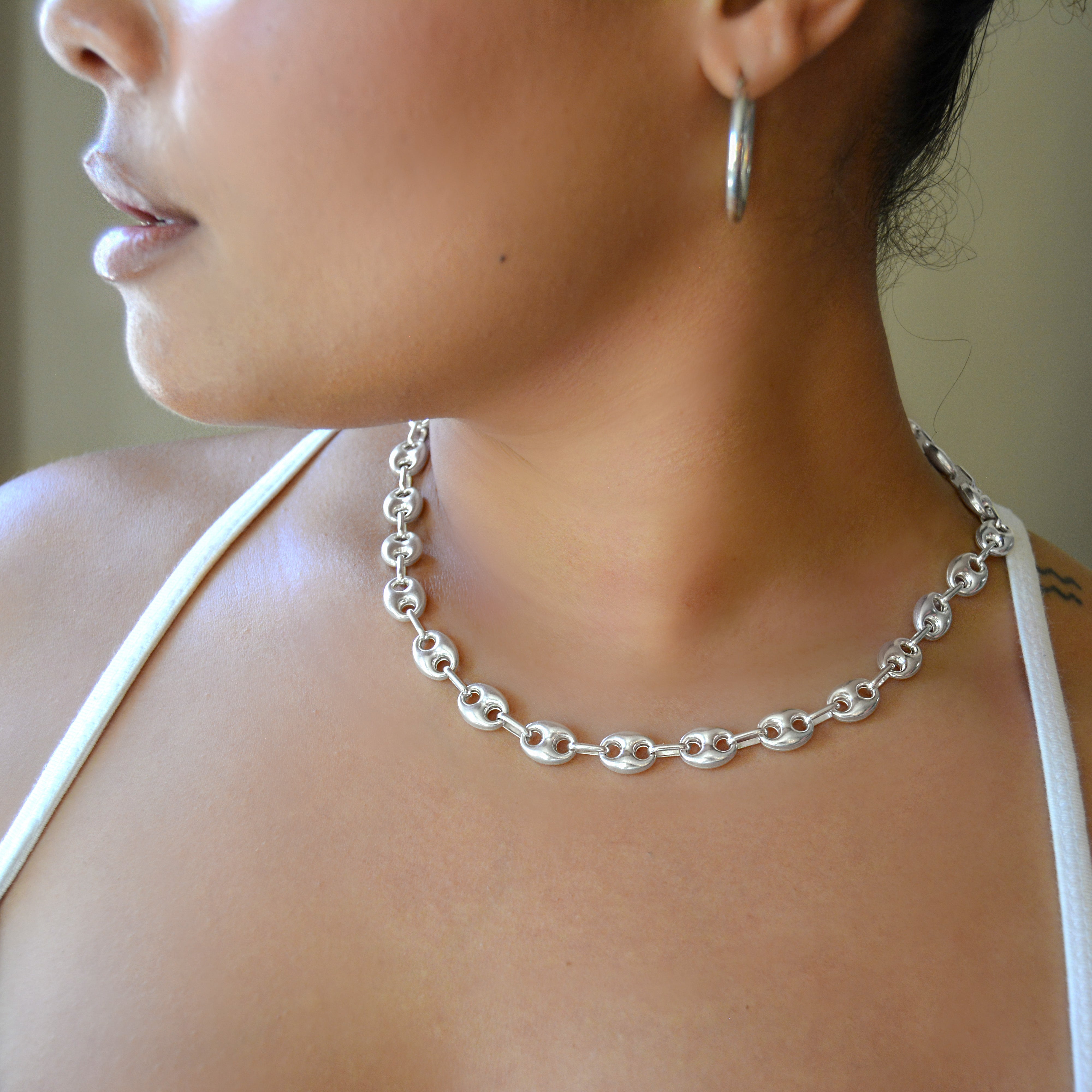 Close-up of a person wearing a silver chain necklace and hoop earring.