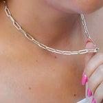 Silver paperclip chain necklace being worn on a person's neck with a close-up view.