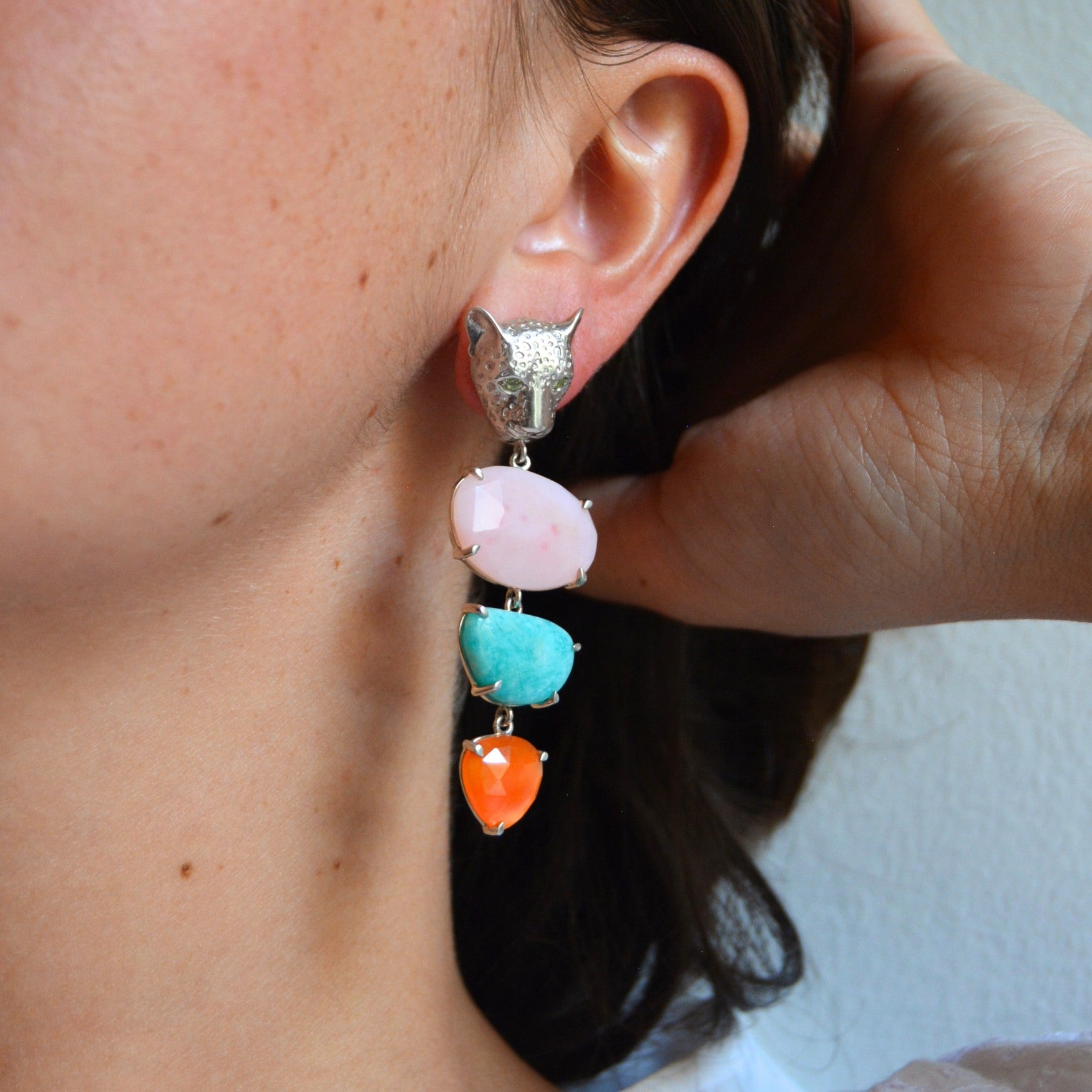 Close-up of a person wearing colorful statement earrings with a neutral background