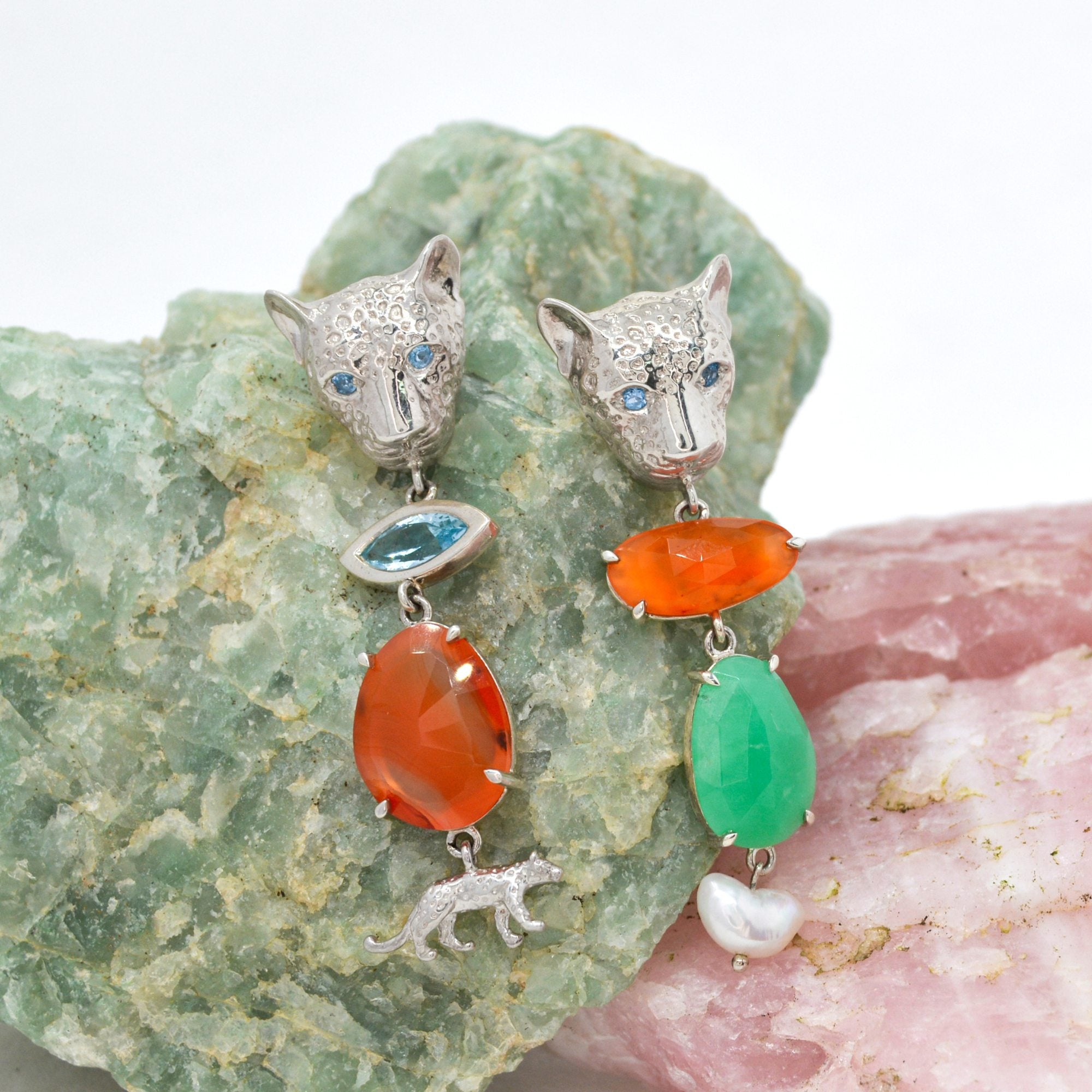 Pair of silver leopard shaped earrings with colorful stones on a textured stone background