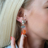Close-up of a person wearing a leopard-themed earring with an orange and blue stone.