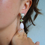 Close-up of a person wearing a unique leopard themed earring with a pink and green stone.