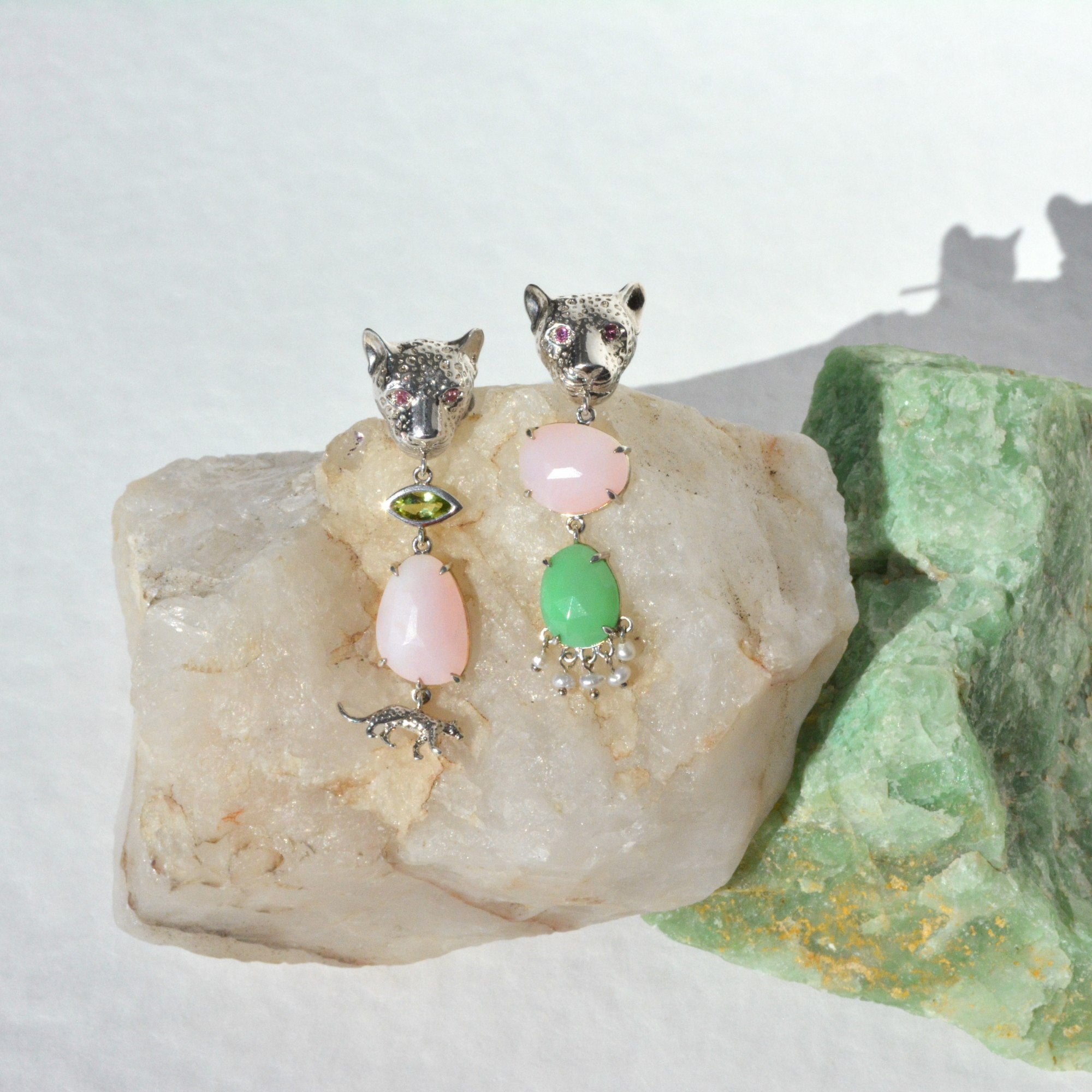 Pair of earrings with leopard-shaped tops and colorful gemstones on a rock with a green stone.
