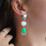 Close-up of an ear wearing a silver earring with green and pink stones.