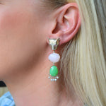 Close-up of an earring with a green, pink and pearly gemstone worn by a person.