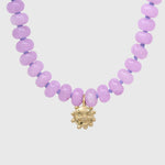 Close-up of the gold smiling sun charm hanging between lilac agate beads on lilac knotted thread