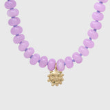 Close-up of the gold smiling sun charm hanging between lilac agate beads on lilac knotted thread