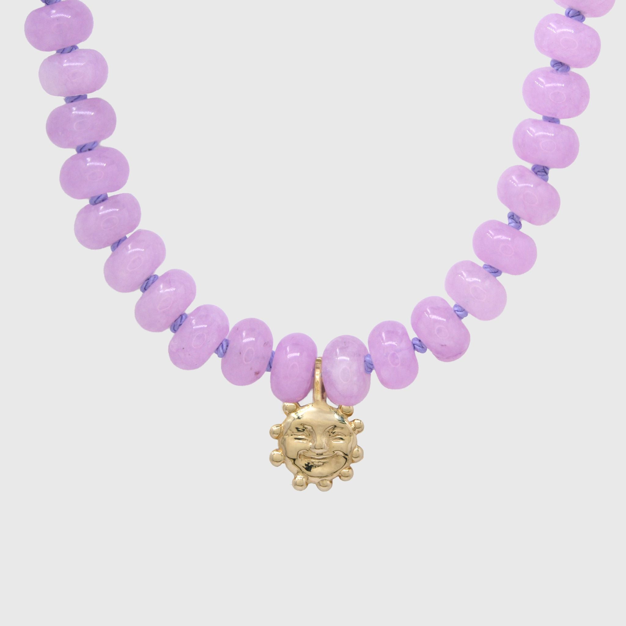 Close-up of the gold smiling sun charm hanging between lilac agate beads on lilac knotted thread