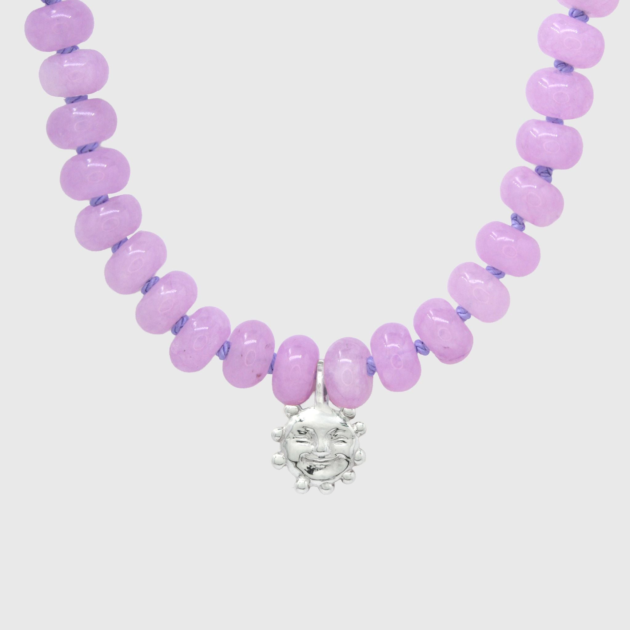 Close-up of the silver smiling sun charm hanging between lilac agate beads on lilac knotted thread