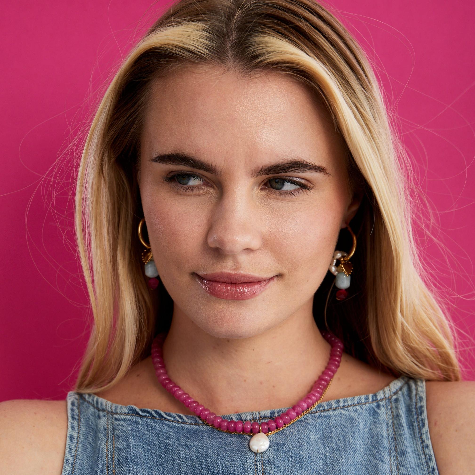 Model against a pink backdrop wearing the pink agate and wonky pearl necklace layered with a gold chain