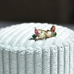 Pair of opal, pink tourmaline and emerald cluster studs in gold, resting on pale blue velvet in sunlight