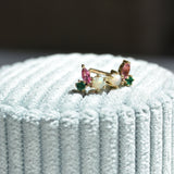 Pair of opal, pink tourmaline and emerald cluster studs in gold, resting on pale blue velvet in sunlight