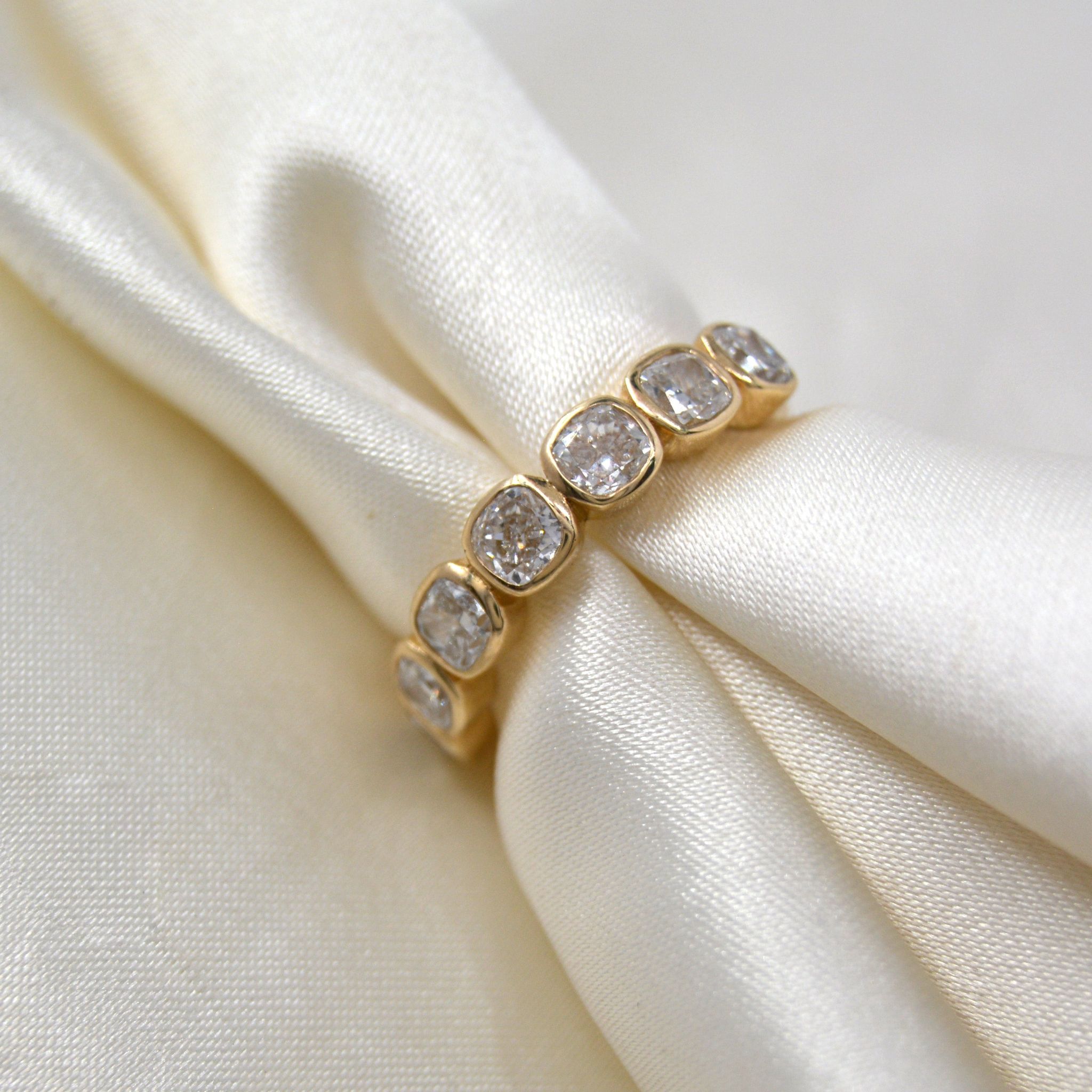 Cushion-cut lab-grown diamond wedding band in 9ct yellow gold, angled on draped ivory satin