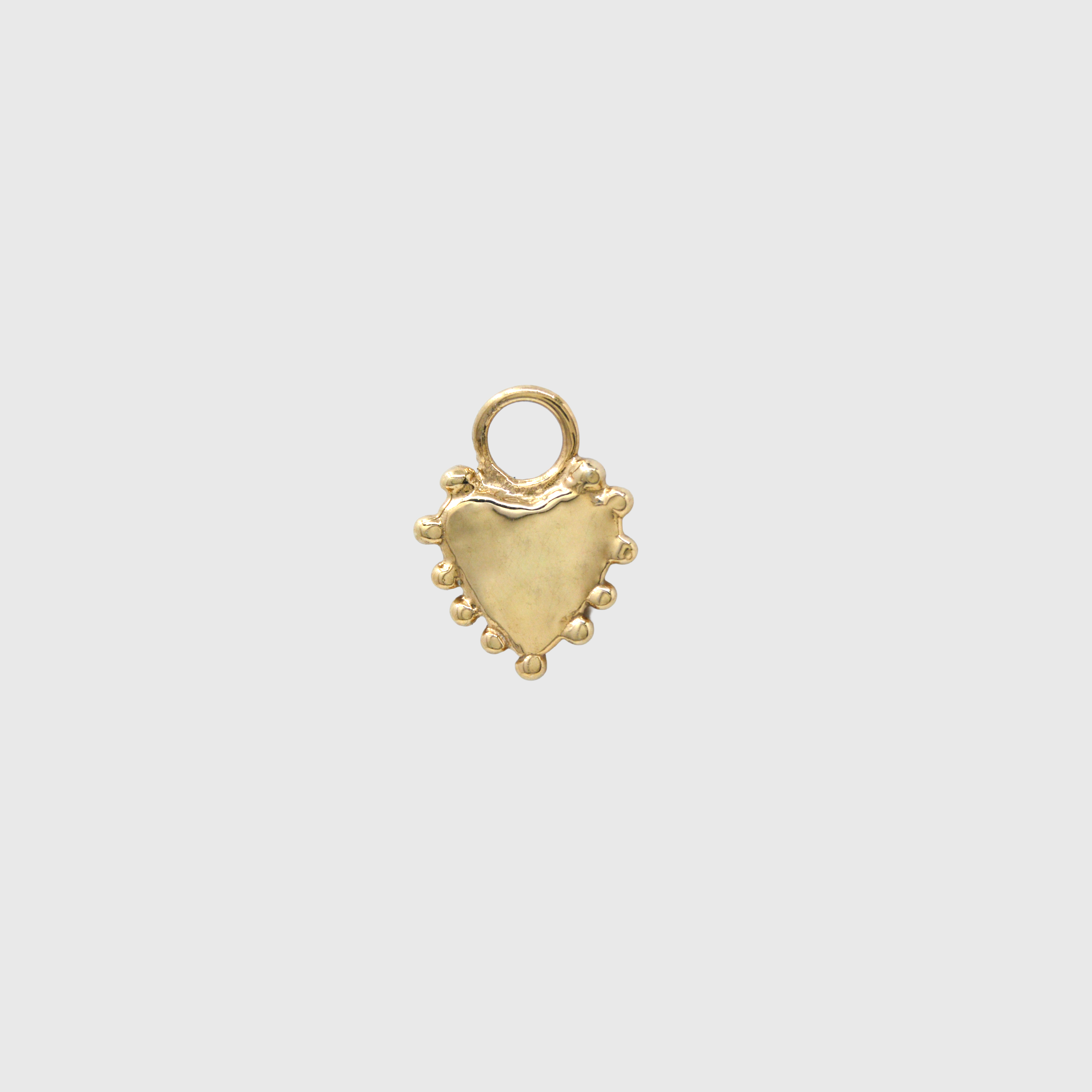 A small gold heart-shaped charm with a textured finish, a loop at the top, and small bead-like details along the bottom edge, centered on a light gray background.