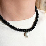 Black beaded necklace with a pearl pendant worn by a person