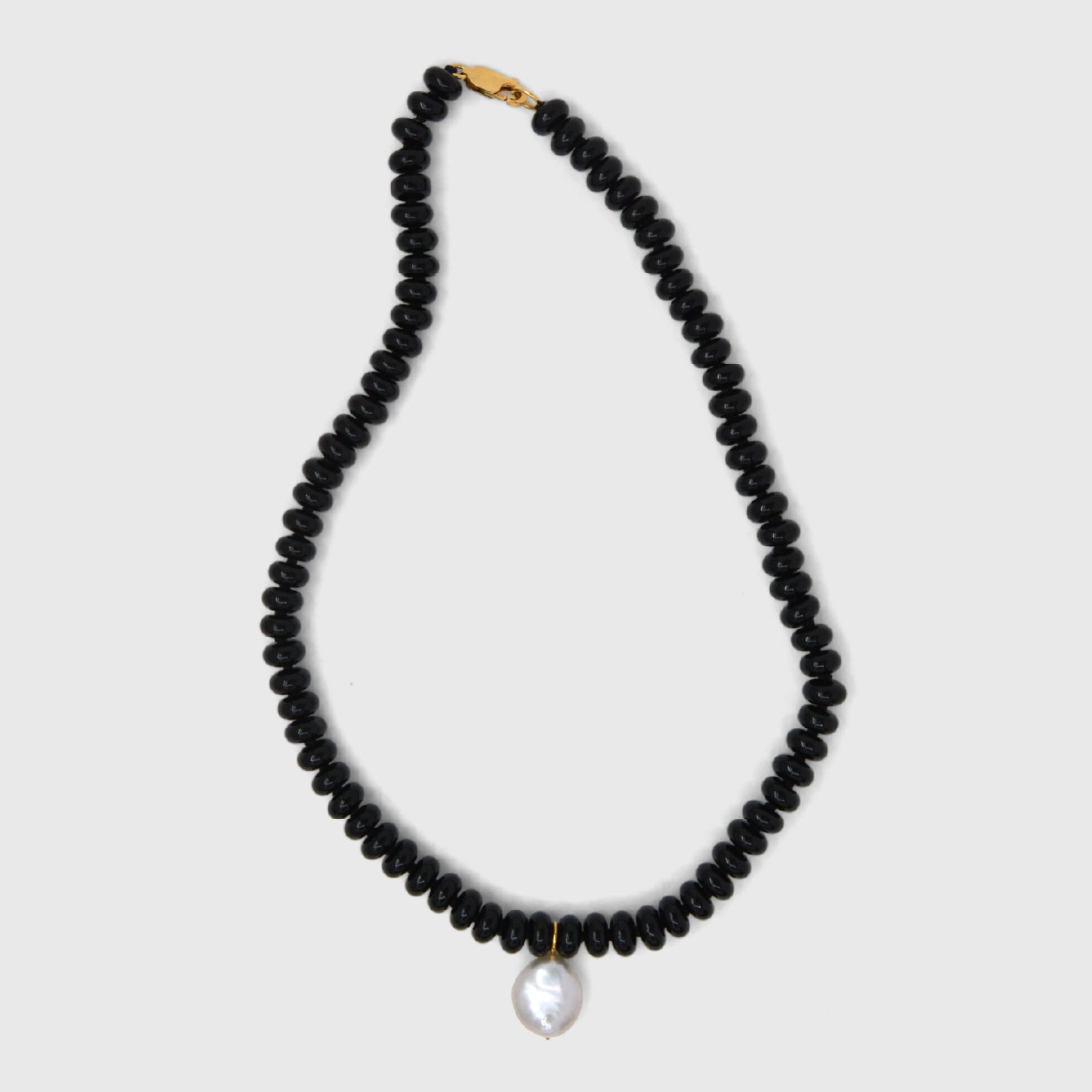 Black beaded necklace with a pearl pendant on a light gray background