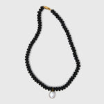 Black beaded necklace with a pearl pendant on a light gray background