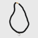 Black beaded necklace with a pearl pendant on a light gray background