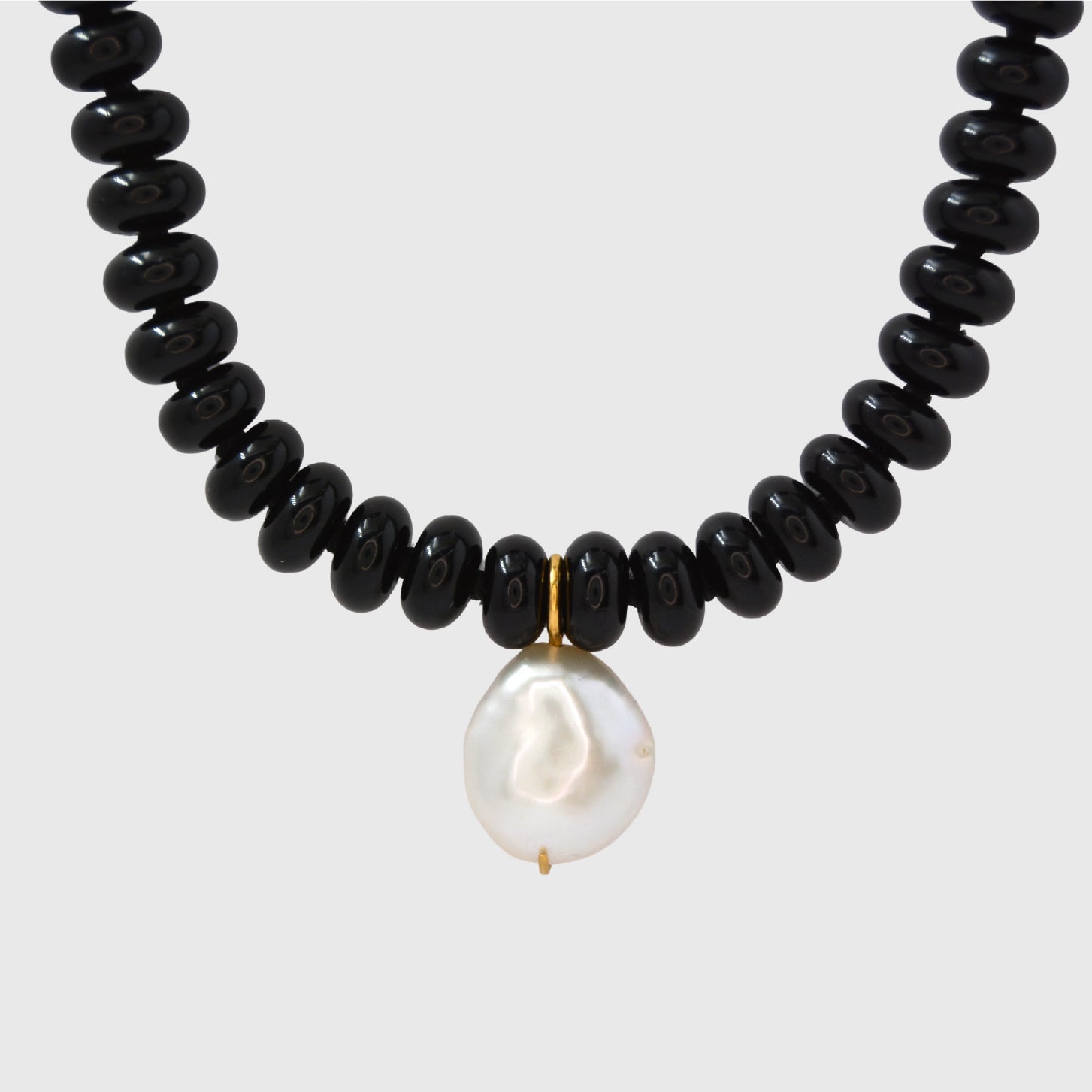Necklace with black beads and a white pearl on a light gray background