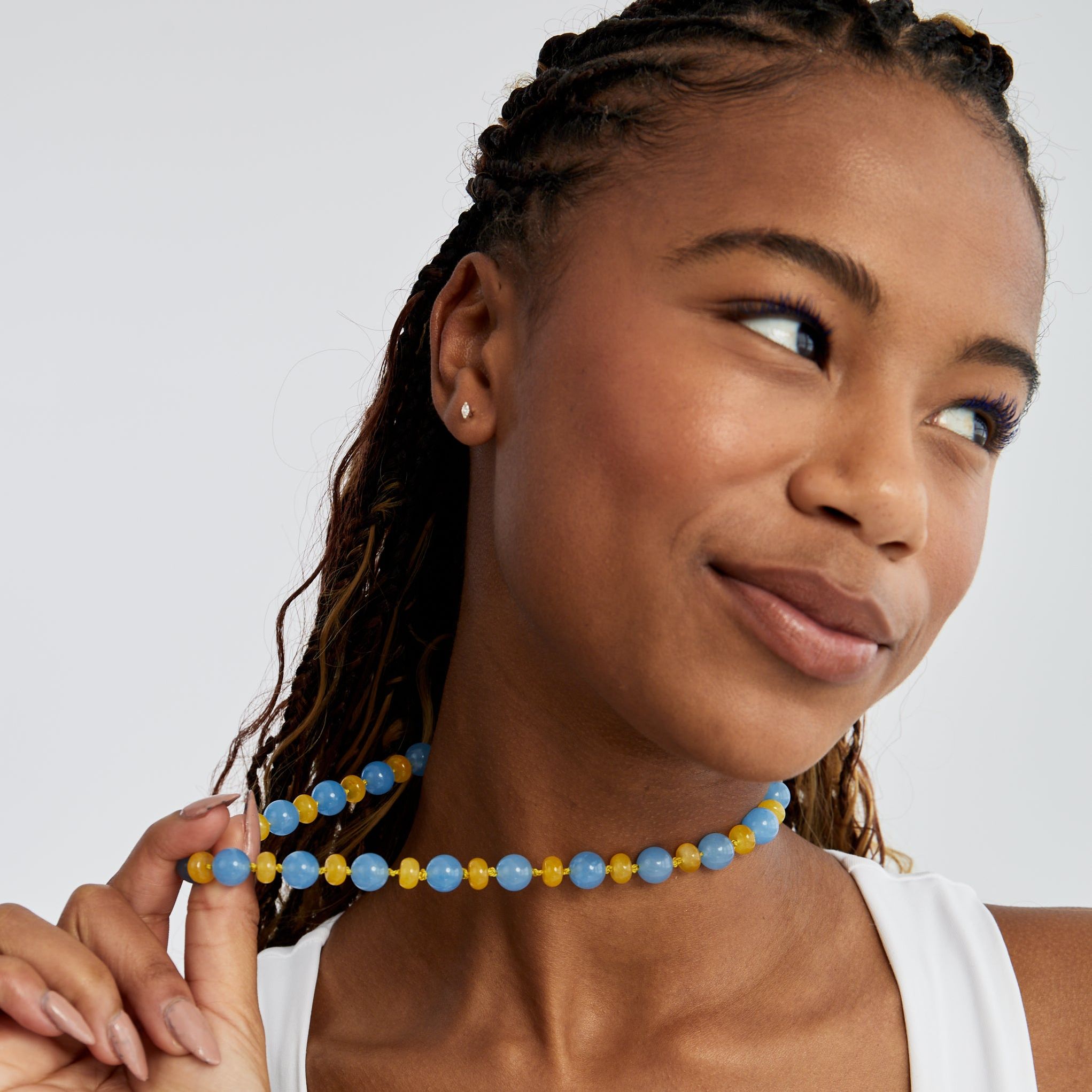Smiling model holding the sky-blue jade and butter-yellow agate necklace away from her neck