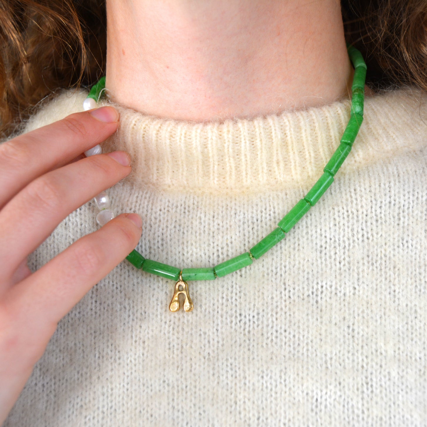 Jade beaded necklace with a gold initial pendant on a woman's neck