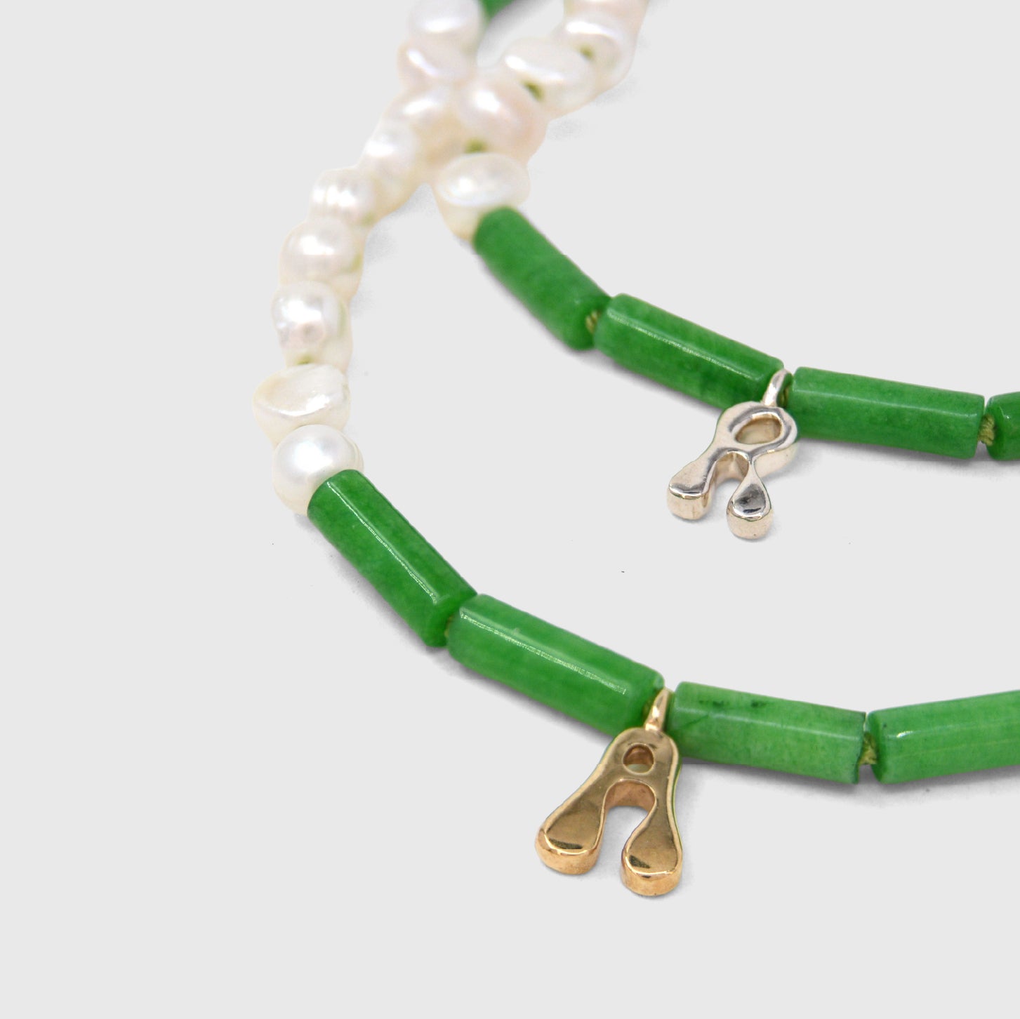 two necklaces with jade and pearl beads with gold and silver initials on white background