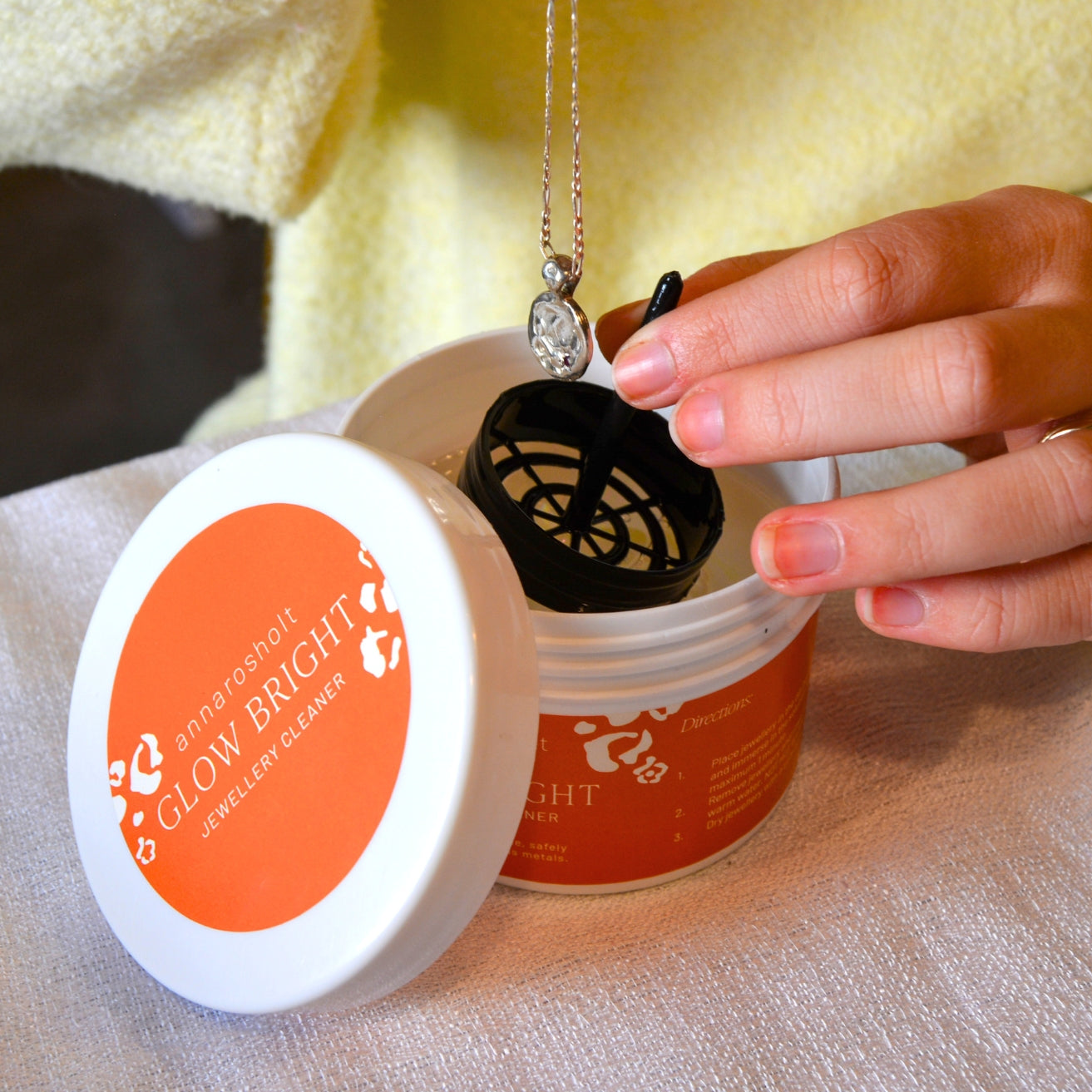 Person using a jewelry cleaner with a necklace inside, on a light fabric background