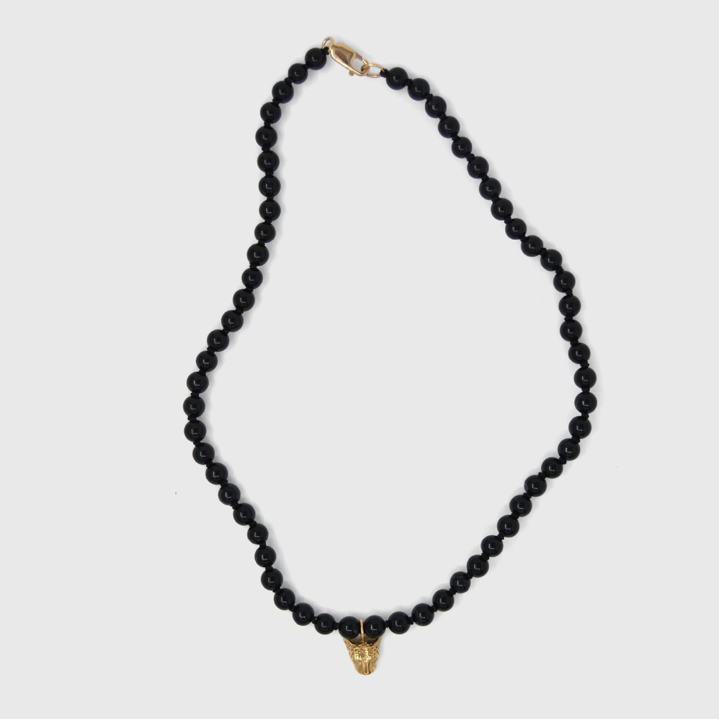 Black beaded necklace with a gold clasp and gold leopard face pendant on a white background