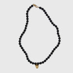 Black beaded necklace with a gold clasp and gold leopard face pendant on a white background
