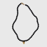 Black beaded necklace with a gold clasp and gold leopard face pendant on a white background