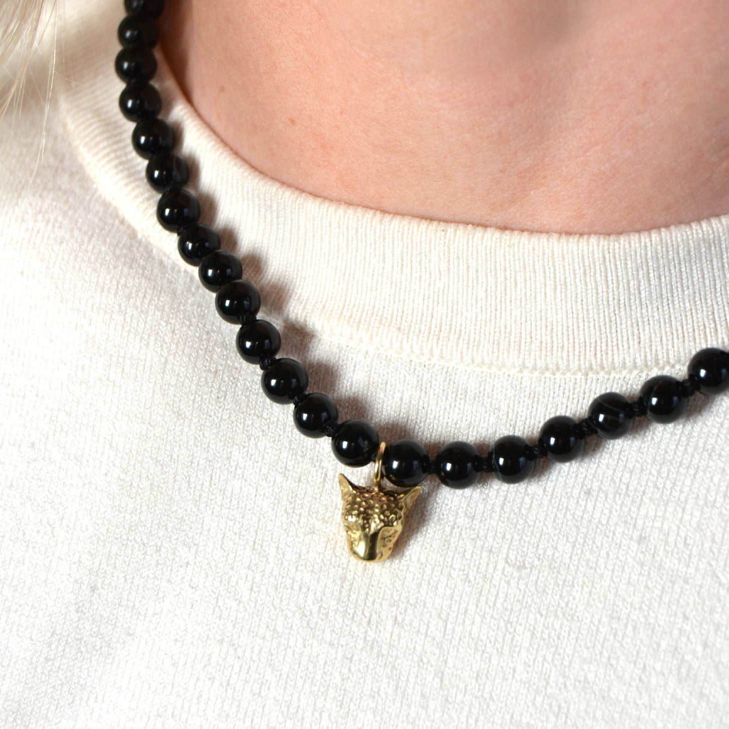 Black beaded necklace with a gold leopard face pendant on a person wearing a white sweater.