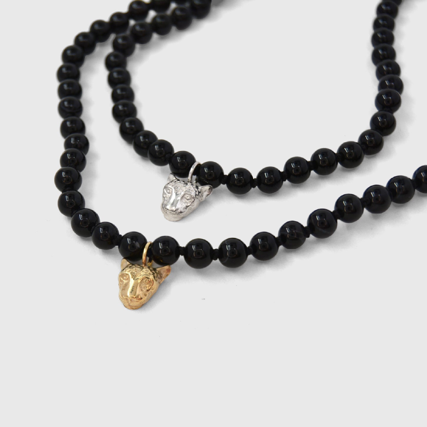 Two black beaded necklaces with gold and silver leopard face pendants on a white background