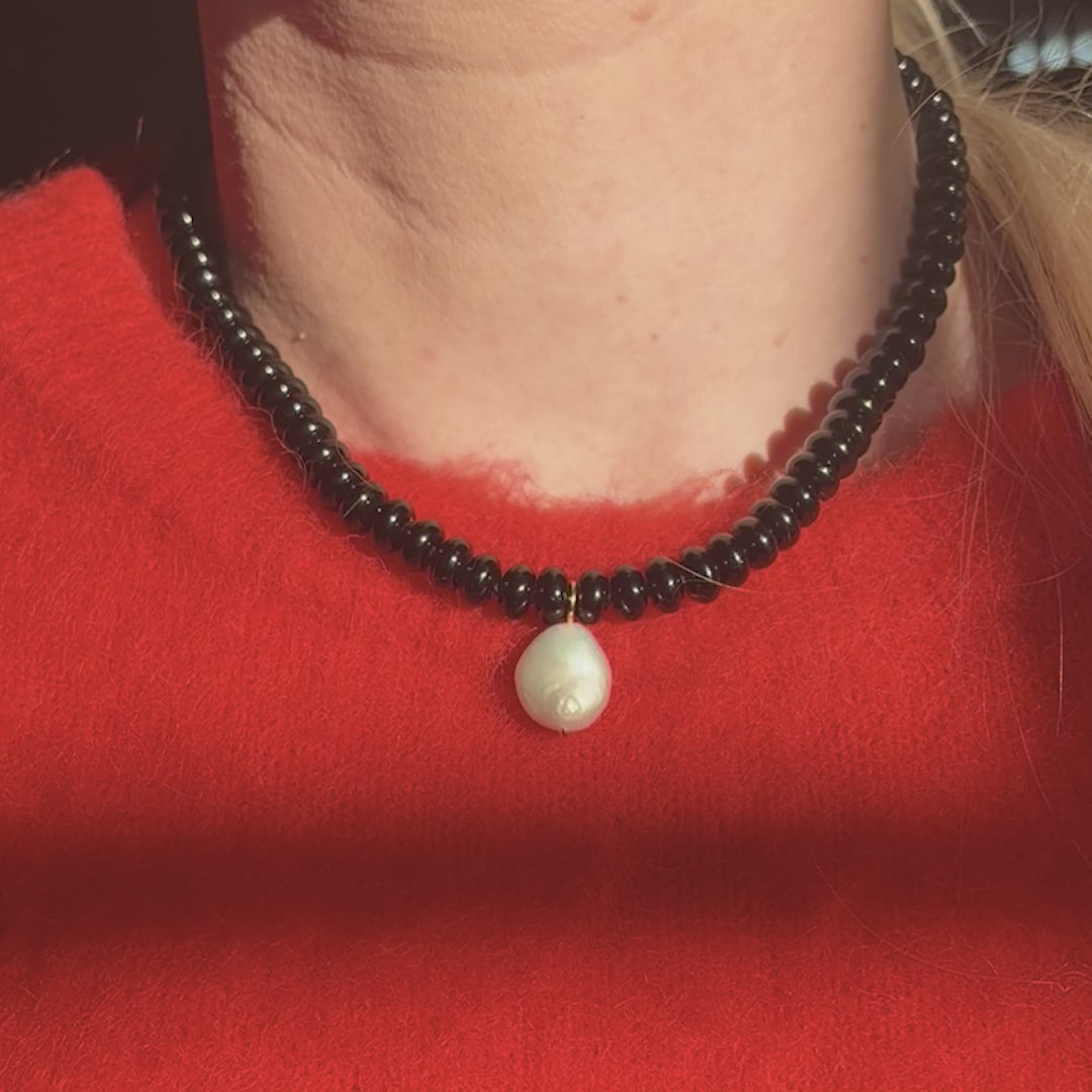 Black beaded necklace with a pearl pendant worn by a person