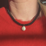 Black beaded necklace with a pearl pendant worn by a person