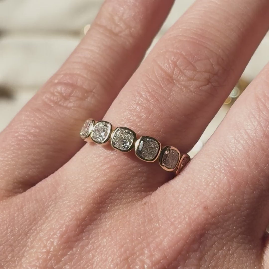 Cushion-cut lab-grown diamond wedding band in 9ct yellow gold, shown on the hand and held up to the light