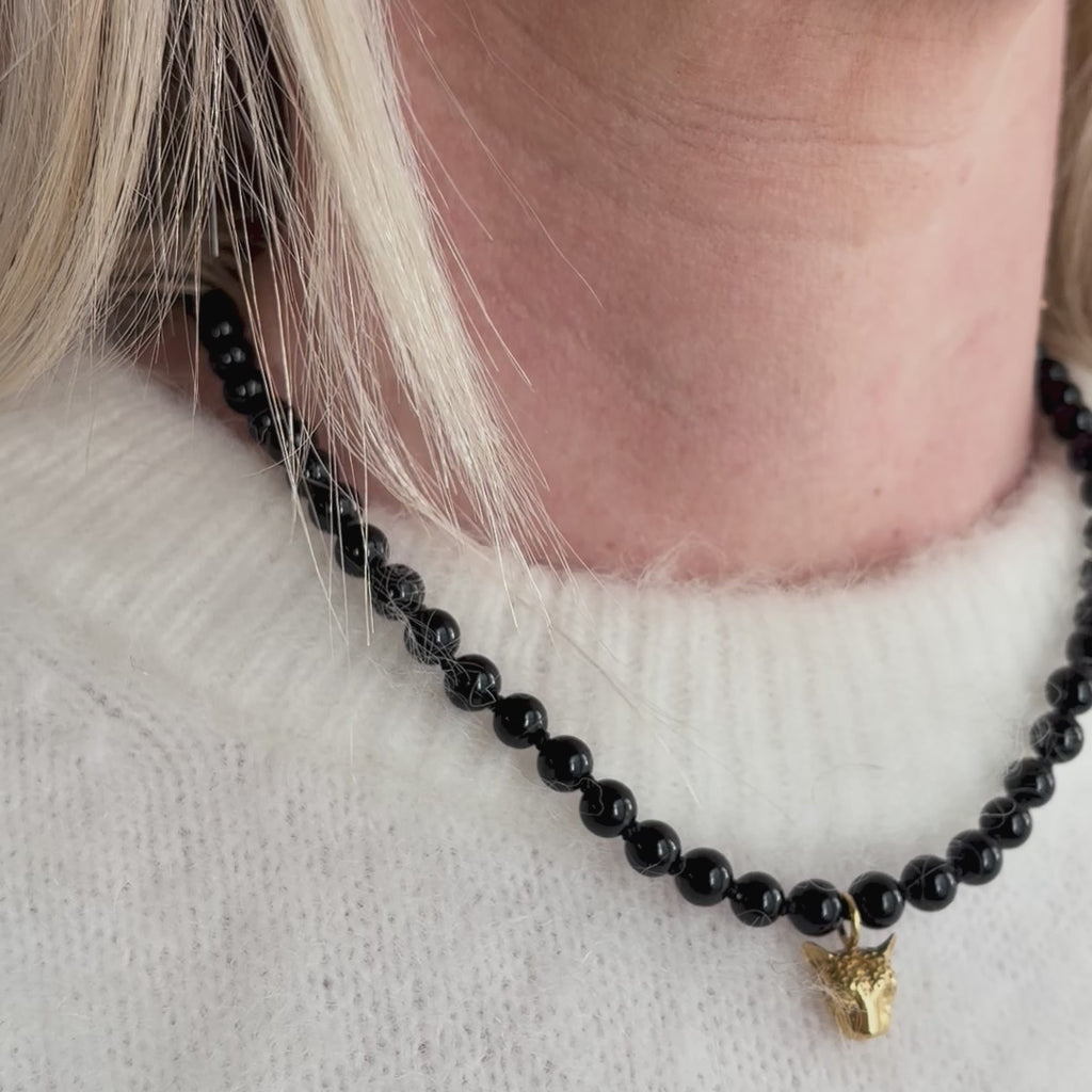 Black beaded necklace with gold leopard face pendant worn around a woman's neck.