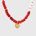 Necklace with coral beads, white pearls, and a gold moon pendant on a light grey background