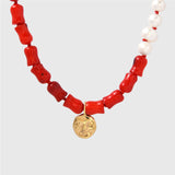 Necklace with coral beads, white pearls, and a gold moon pendant on a light grey background