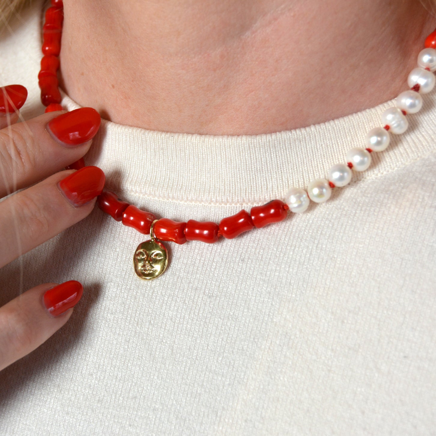 Necklace with coral beads and a gold  moon charm worn by a person 