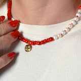 Necklace with coral beads and a gold  moon charm worn by a person 
