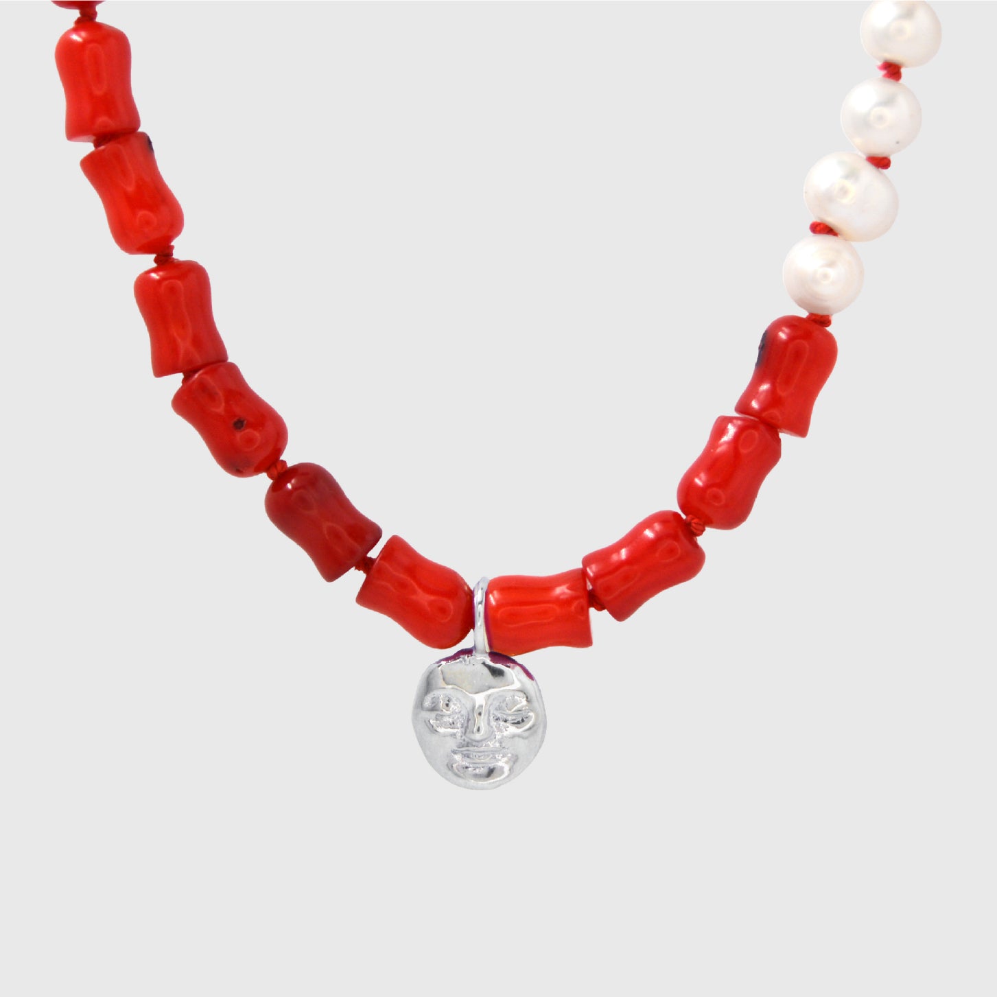 Necklace with coral and pearl beads with a silver moon pendant on a light grey background