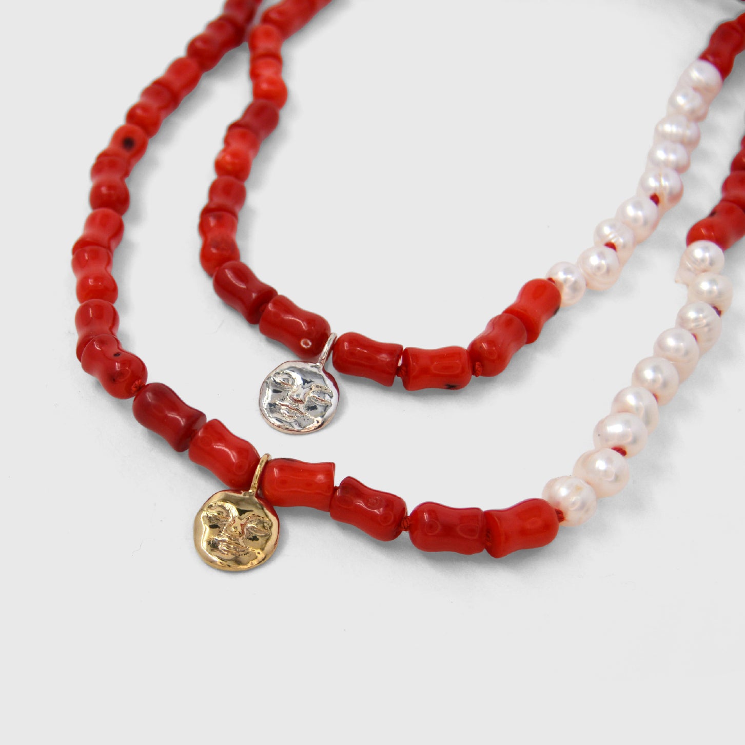 Two necklaces with coral and pearl beads and gold moon charms on a white background