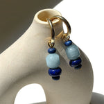 Pair of aquamarine and lapis lazuli charms on gold hoops, hung on a ceramic vase in sunlight