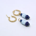 Two aquamarine and lapis lazuli charms, one hung on a gold hoop earring and one lying beside an open hoop