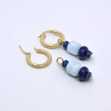 Two aquamarine and lapis lazuli charms, one hung on a gold hoop earring and one lying beside an open hoop